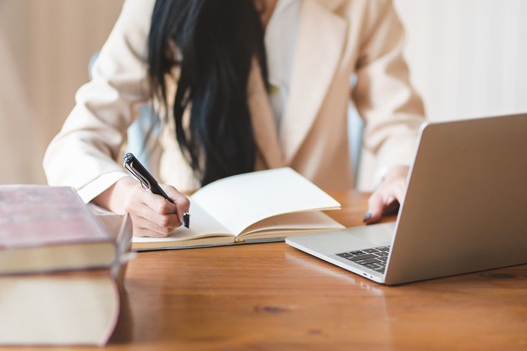 A person studying for CELPIP, taking notes on a notebook while using a laptop