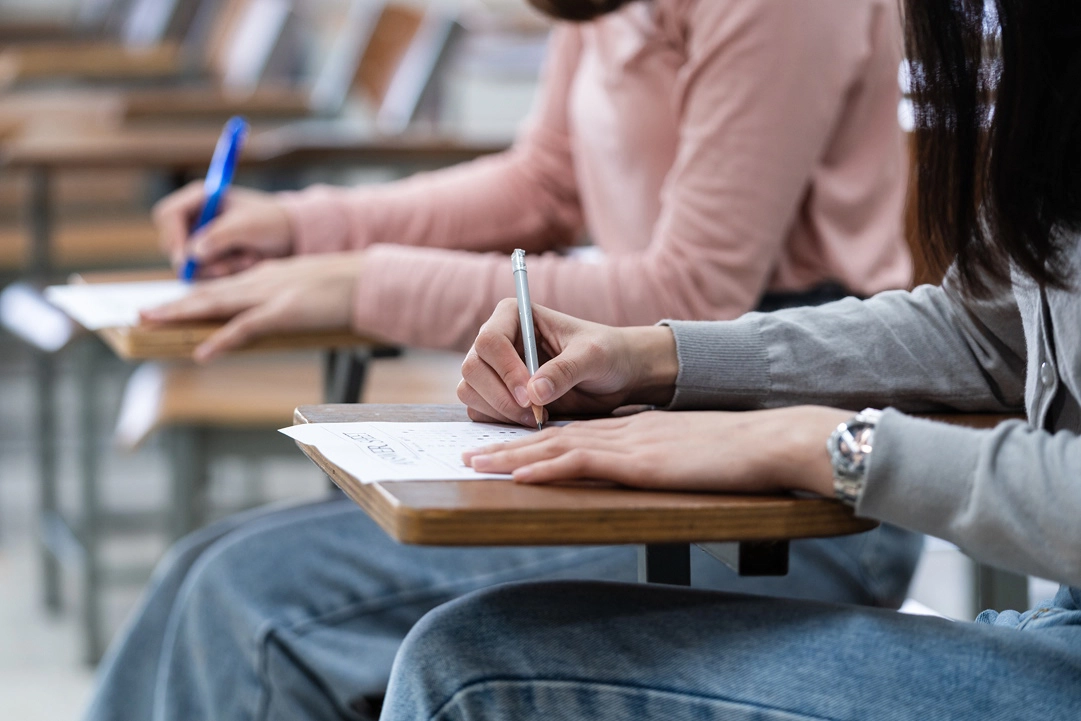 Two young adults seated at desks take tests.